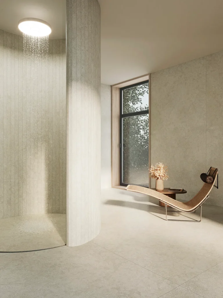 Espacio minimalista con suelo y paredes en Amaya Linen, piedra sinterizada de Ascale, que refleja la calma de la piedra natural. Una silla reclinable de diseño moderno y una escultura de madera añaden calidez y personalidad al rincón, mientras la luz natural entra por la ventana, resaltando los suaves matices y la textura del material.